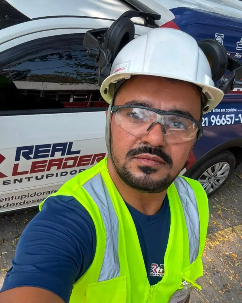 Profissional da Real Leader Desentupidora de capacete e colete ao lado do carro da empresa